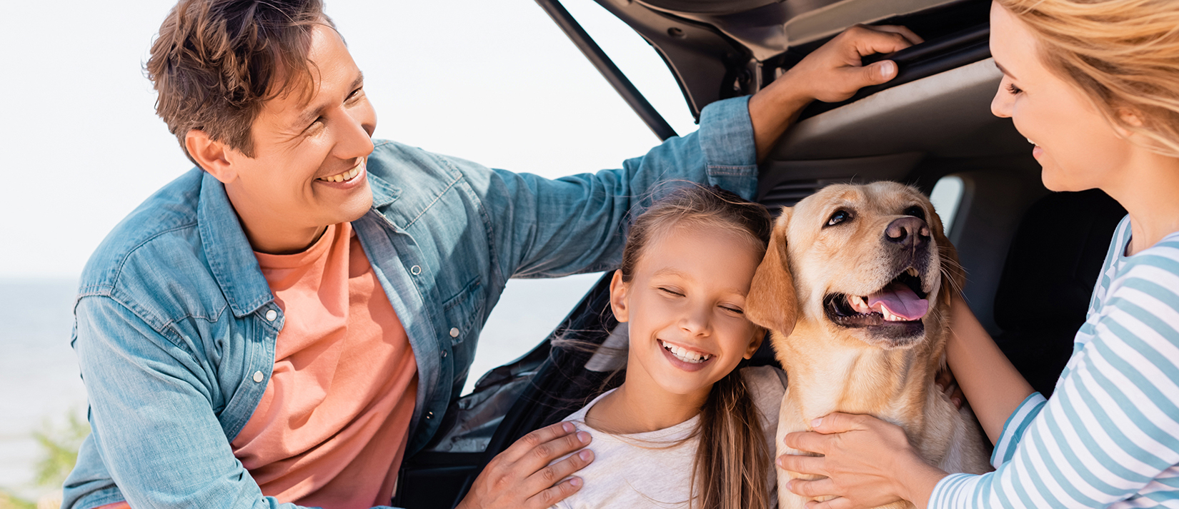 Horizontal crop of family with golden retriever standing near auto on beach